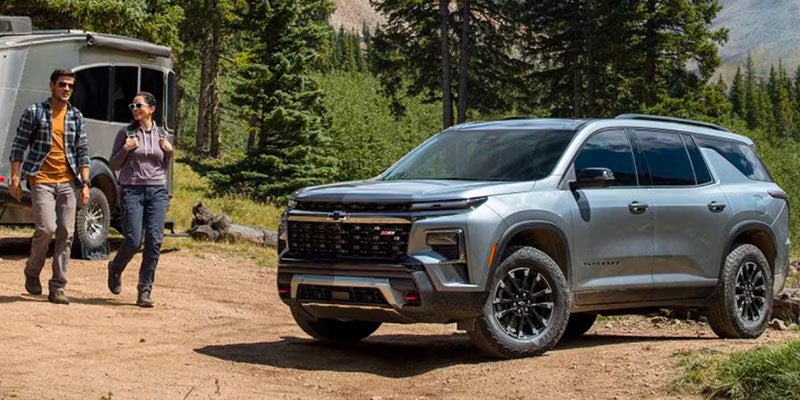 A SUV parked on graound and a men and women walking while communicating